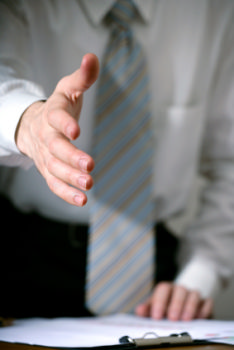 This photo shows a man leaning over a desk to shake hands. This job seekers is being welcomed to their new job after following this article's advice